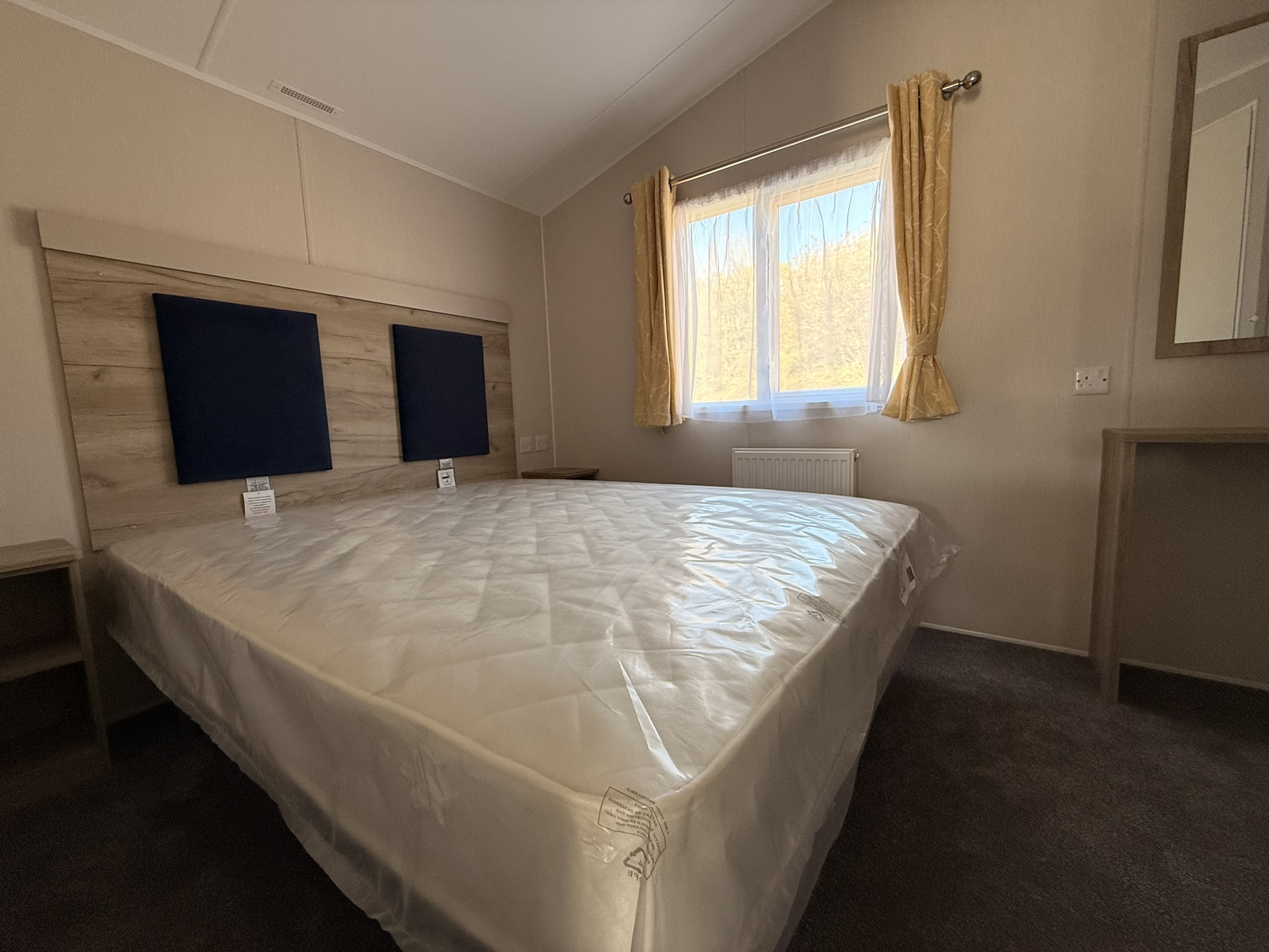 Modern bedroom with double bed, wooden headboard, golden curtains, and bright window.