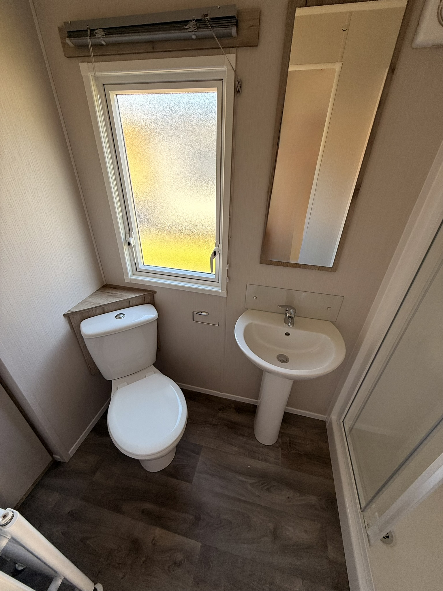 Small bathroom interior with toilet, pedestal sink, frosted window, and beige walls
