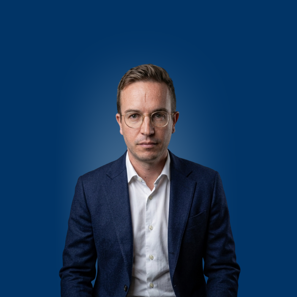 Portrait of a young woman with long blonde hair and glasses wearing a light blue shirt.