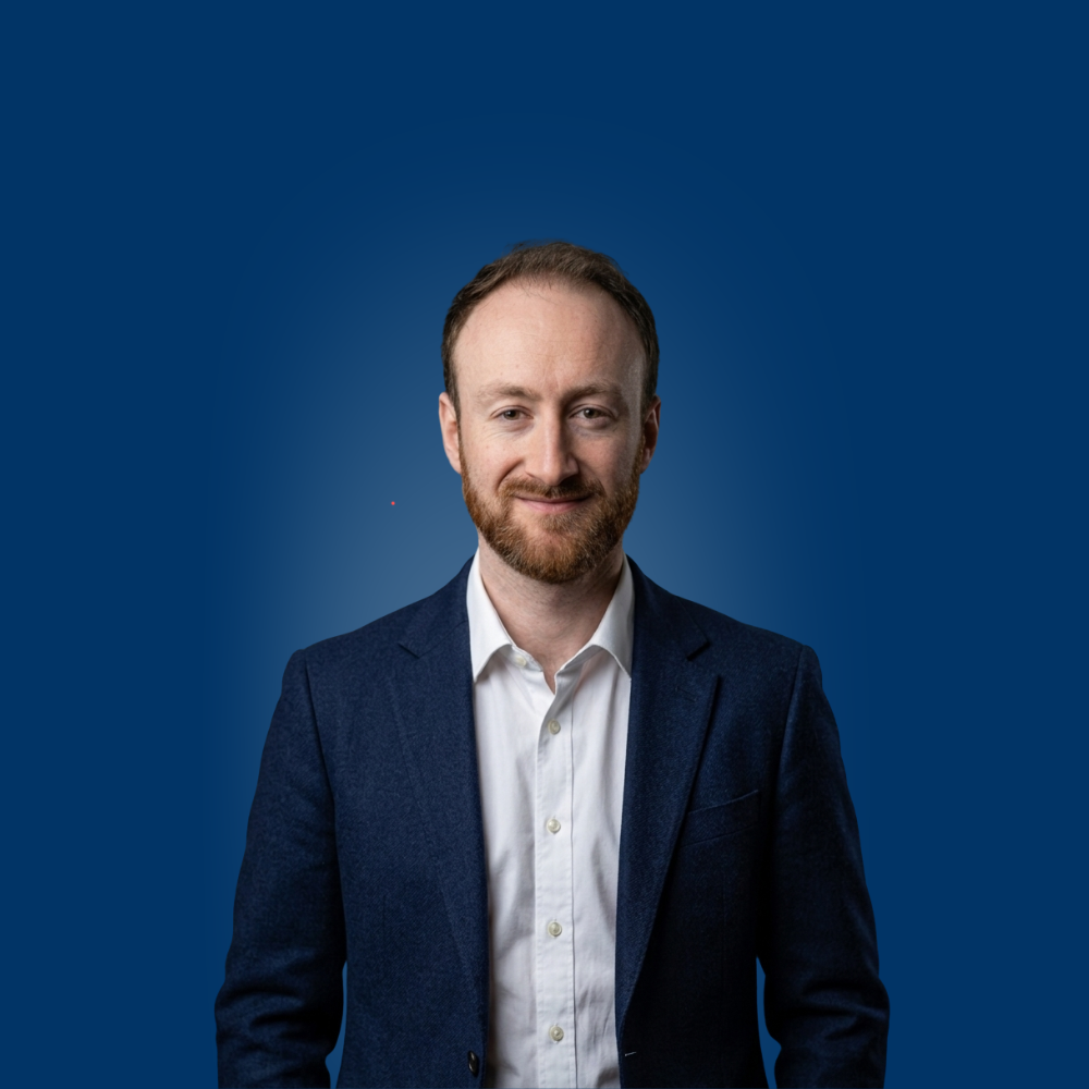 Portrait of a young woman with long blonde hair and glasses wearing a light blue shirt.