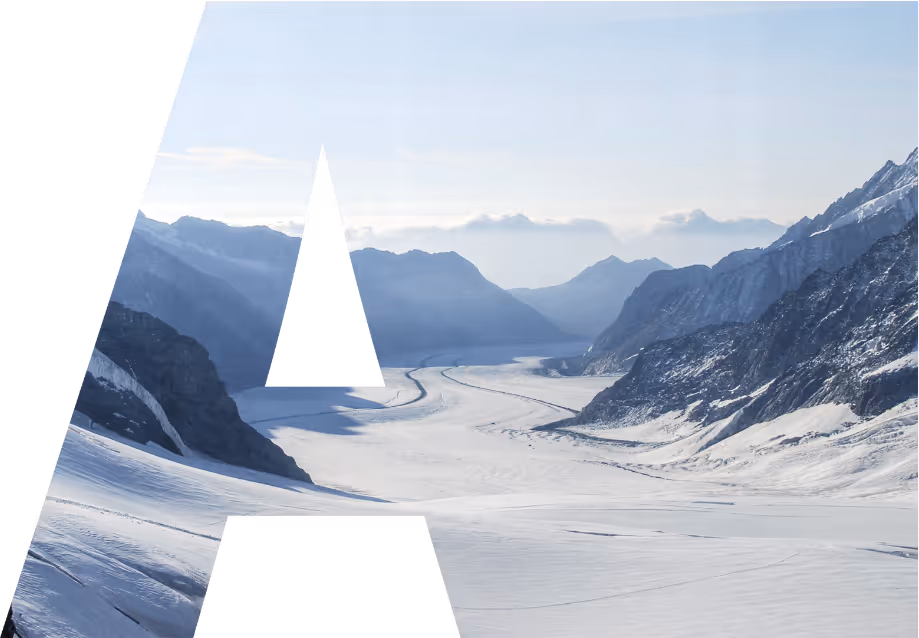 Snow-covered mountain valley under a clear sky with layered mountain ridges in the background.