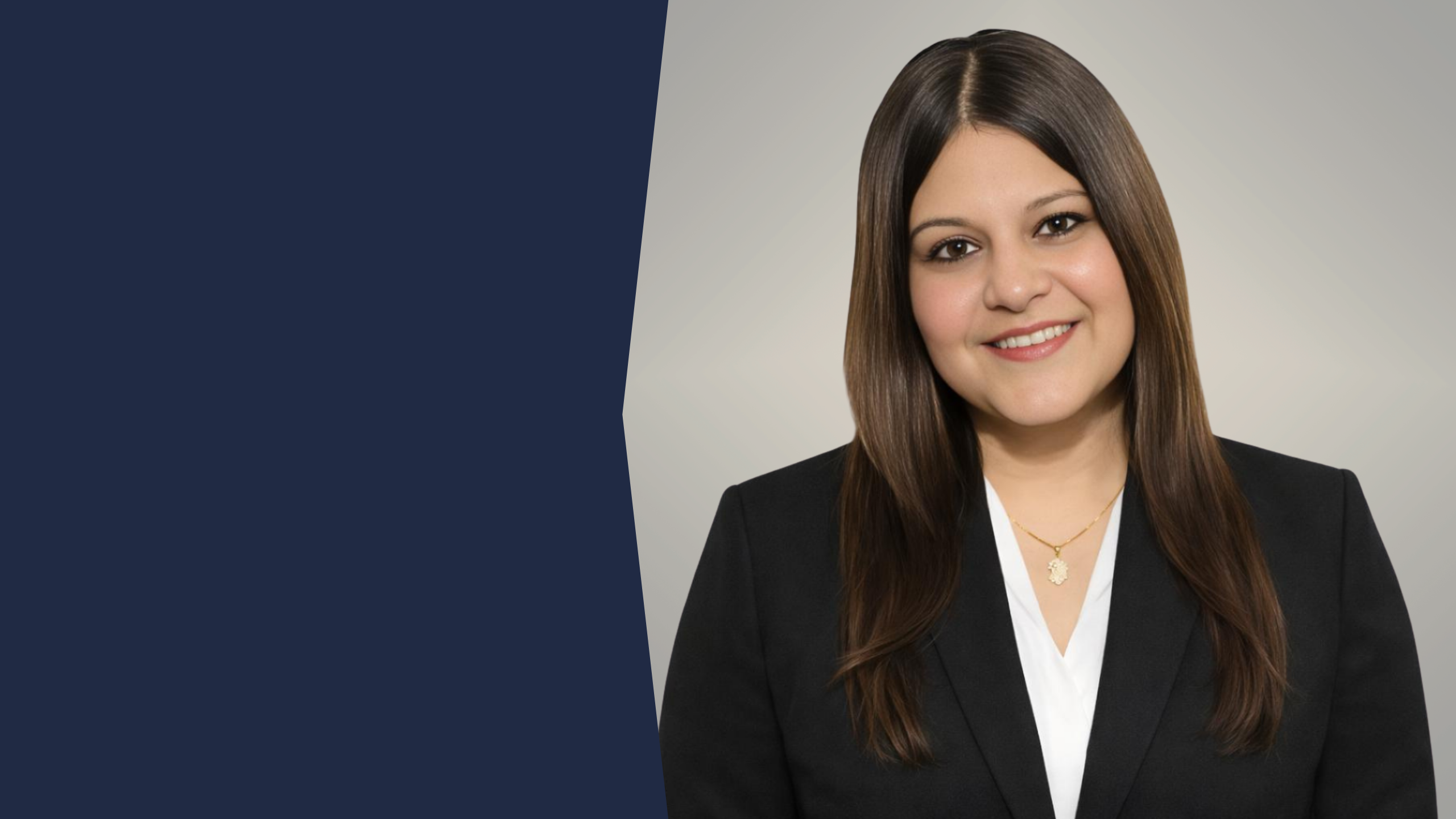 Woman with long brown hair wearing a floral jacket and smiling indoors with blurred background.