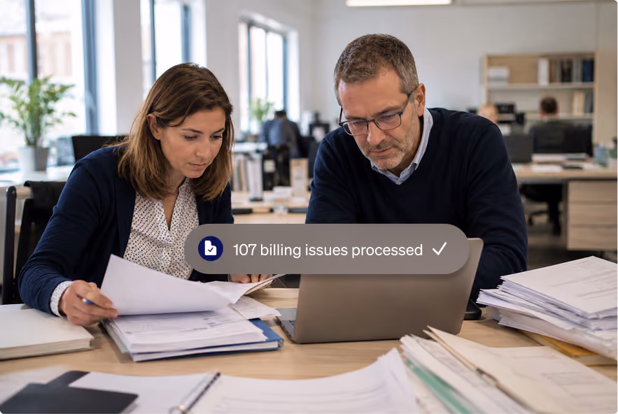 Two colleagues reviewing paperwork and working together on billing documents at a desk.