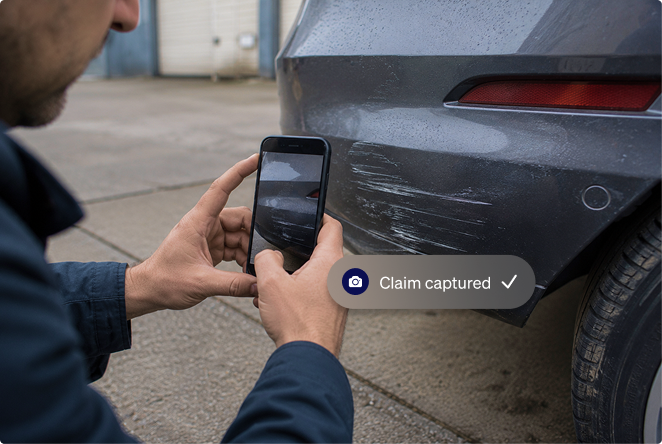 Person using a smartphone to photograph vehicle damage for an insurance claim.