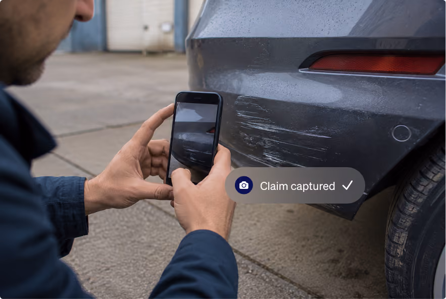Person photographing vehicle damage on a car bumper with a smartphone for a digital insurance claim.