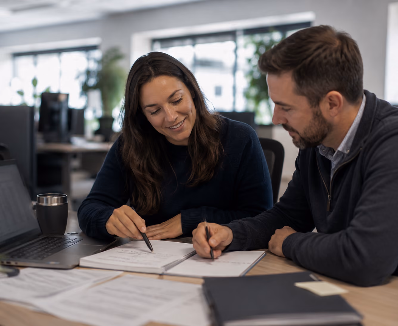Man and woman sitting at a desk reviewing documents together with a laptop in an office.