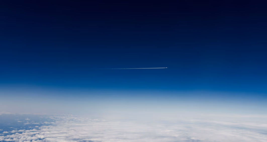 Airplane flying above the clouds with a contrail across a clear blue sky.