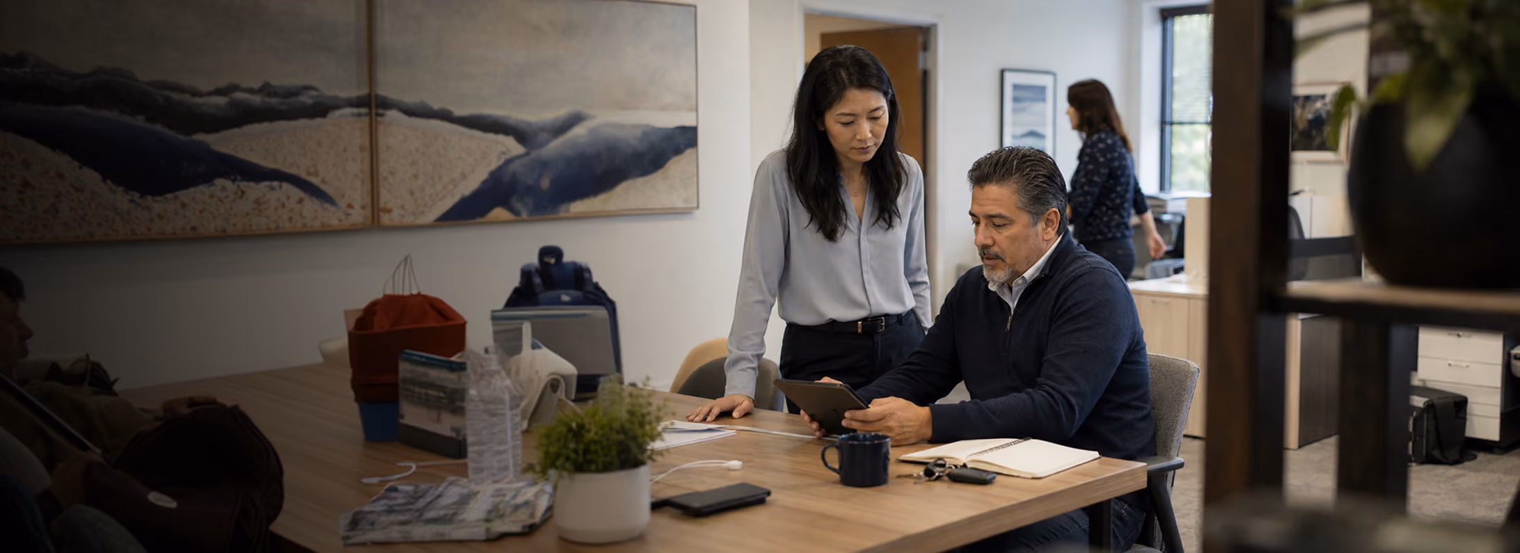 Business professionals reviewing documents during a meeting in a modern glass-walled conference room.