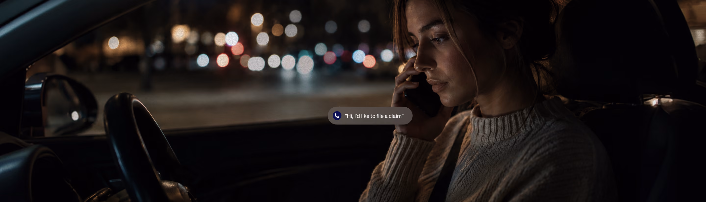 Woman in car at night talking on phone with blurred city lights visible through window.