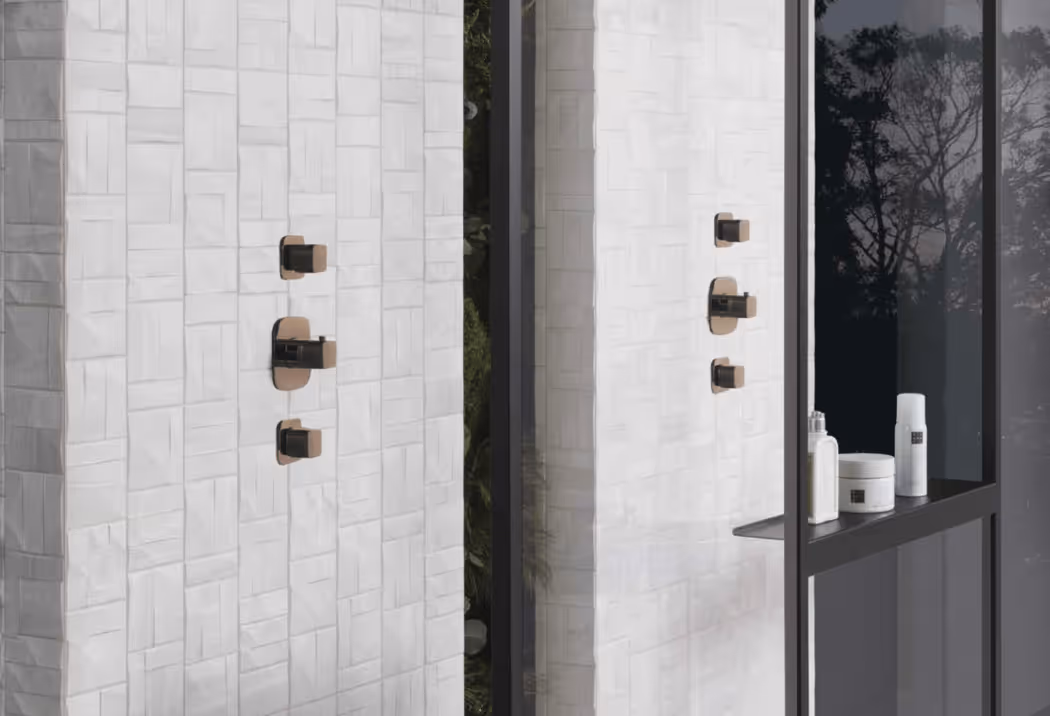 Porcelanosa witte structuurtegel met bronskleurige kranen en verzorgingsproducten