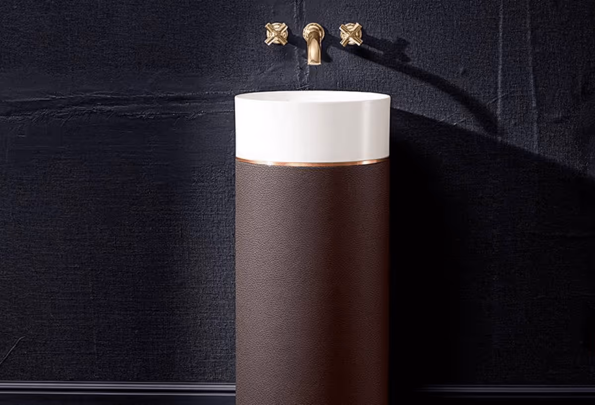 Villeroy & Boch wastafel met bruin lederen sokkel en gouden kruiskraan tegen zwarte wand