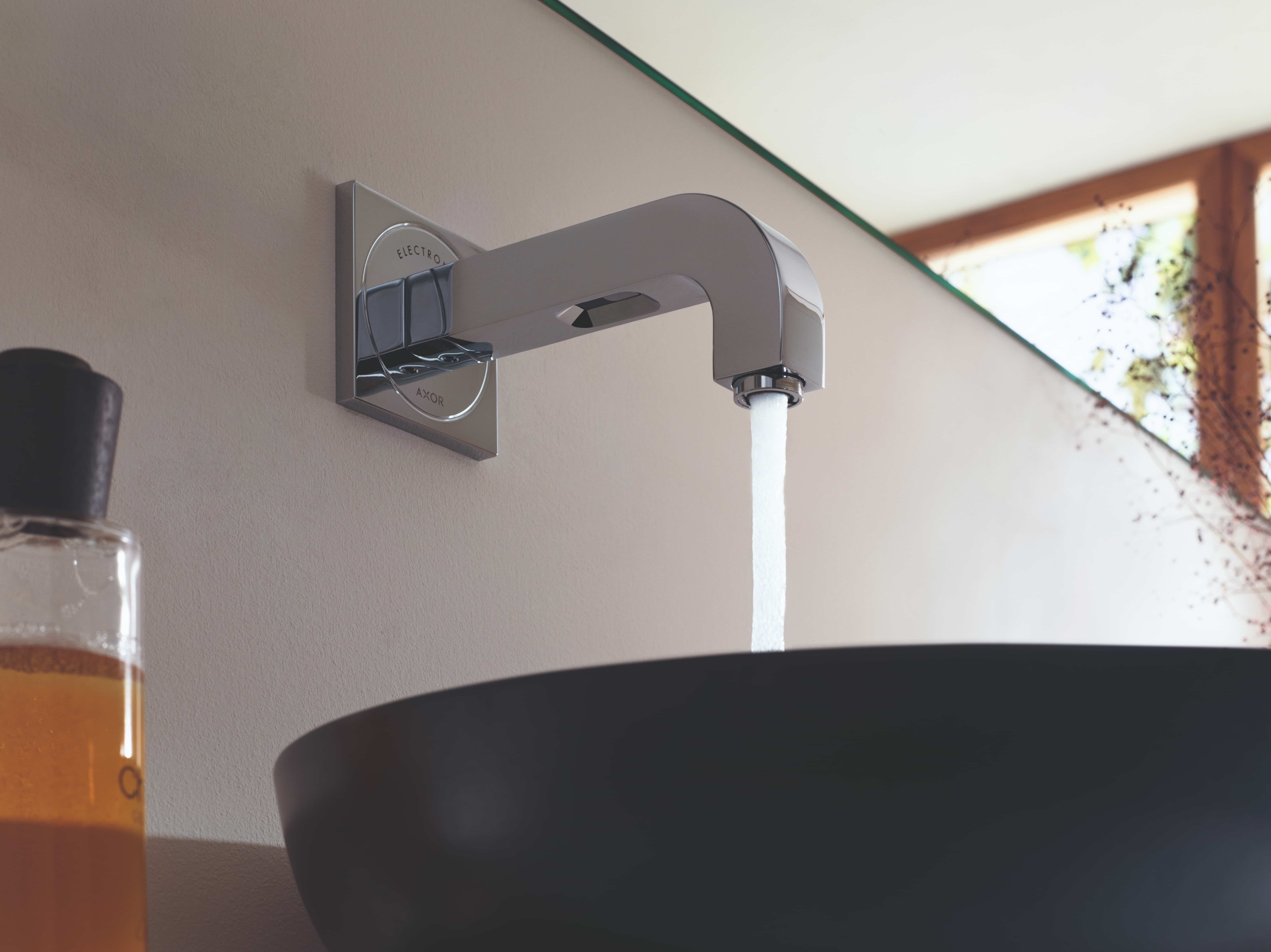 Axor Citterio wandkraan in chroom met stromend water boven zwarte waskom