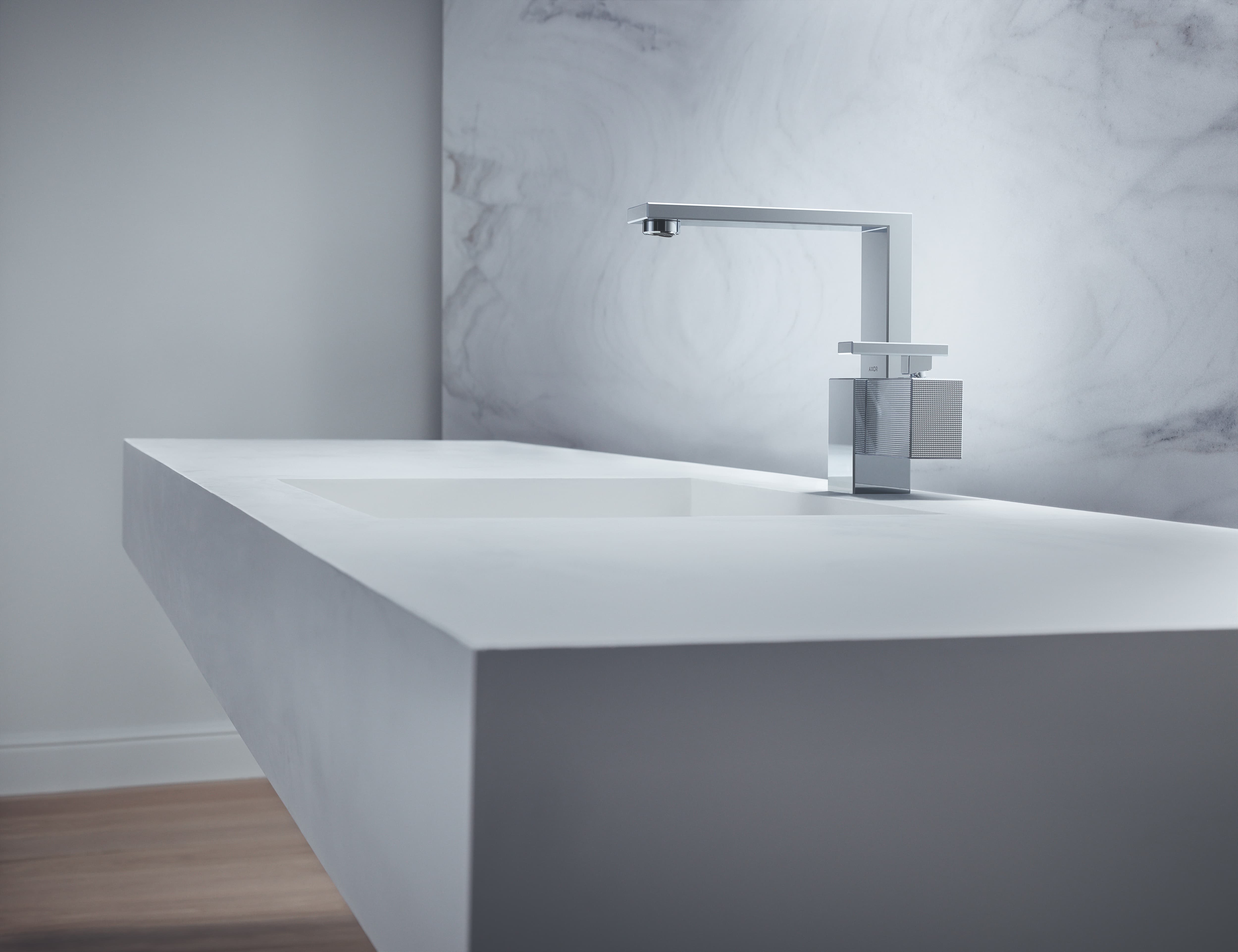 Axor Edge wastafelkraan naast wit wastafelblad tegen marmeren wand