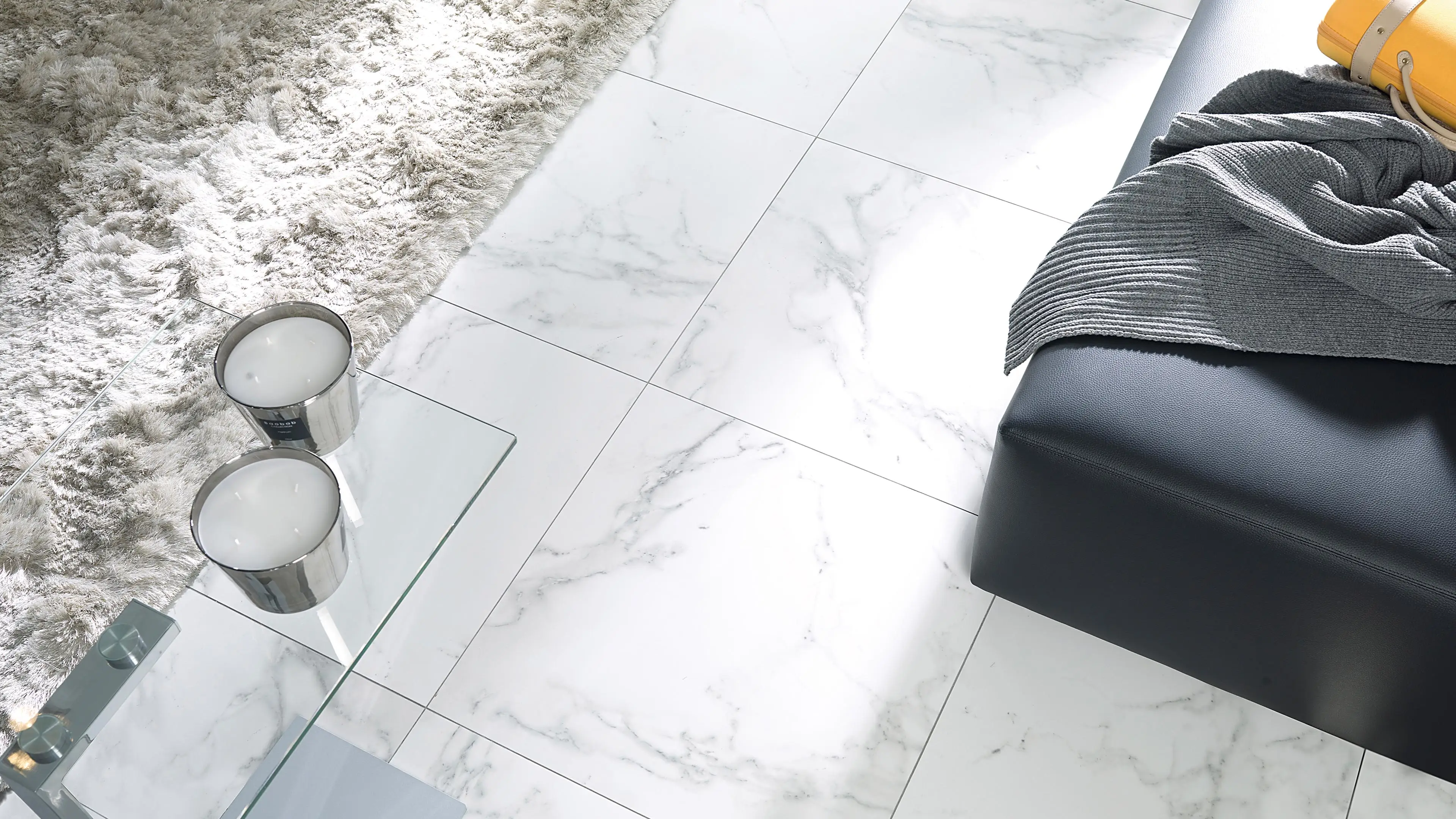 Porcelanosa Carrara Blanco Pulido marmerlook tegelvloer in woonruimte met zwarte poef en vloerkleed