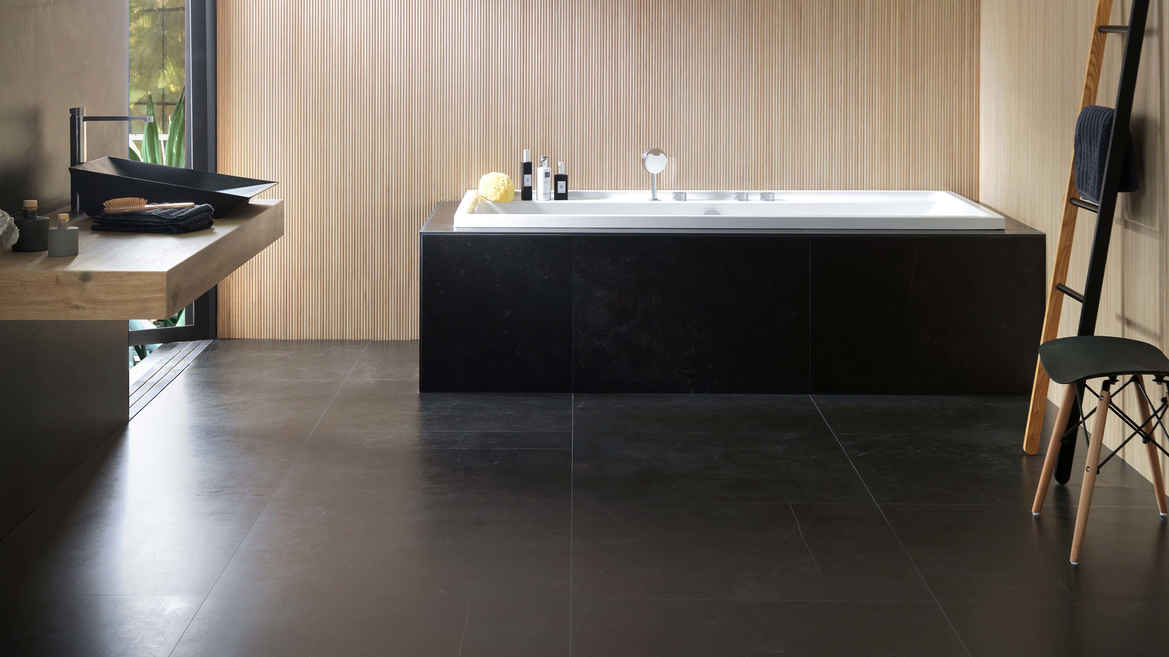Badkamer met Porcelanosa Magma Black tegel op vloer en badpaneel, houten wastafelmeubel