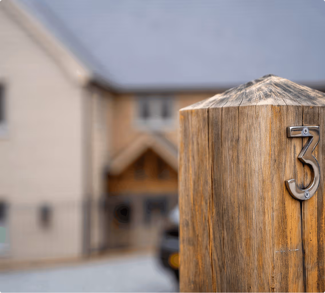 Close-up of a wooden post with the number 3 mounted on it, house blurred in the background.