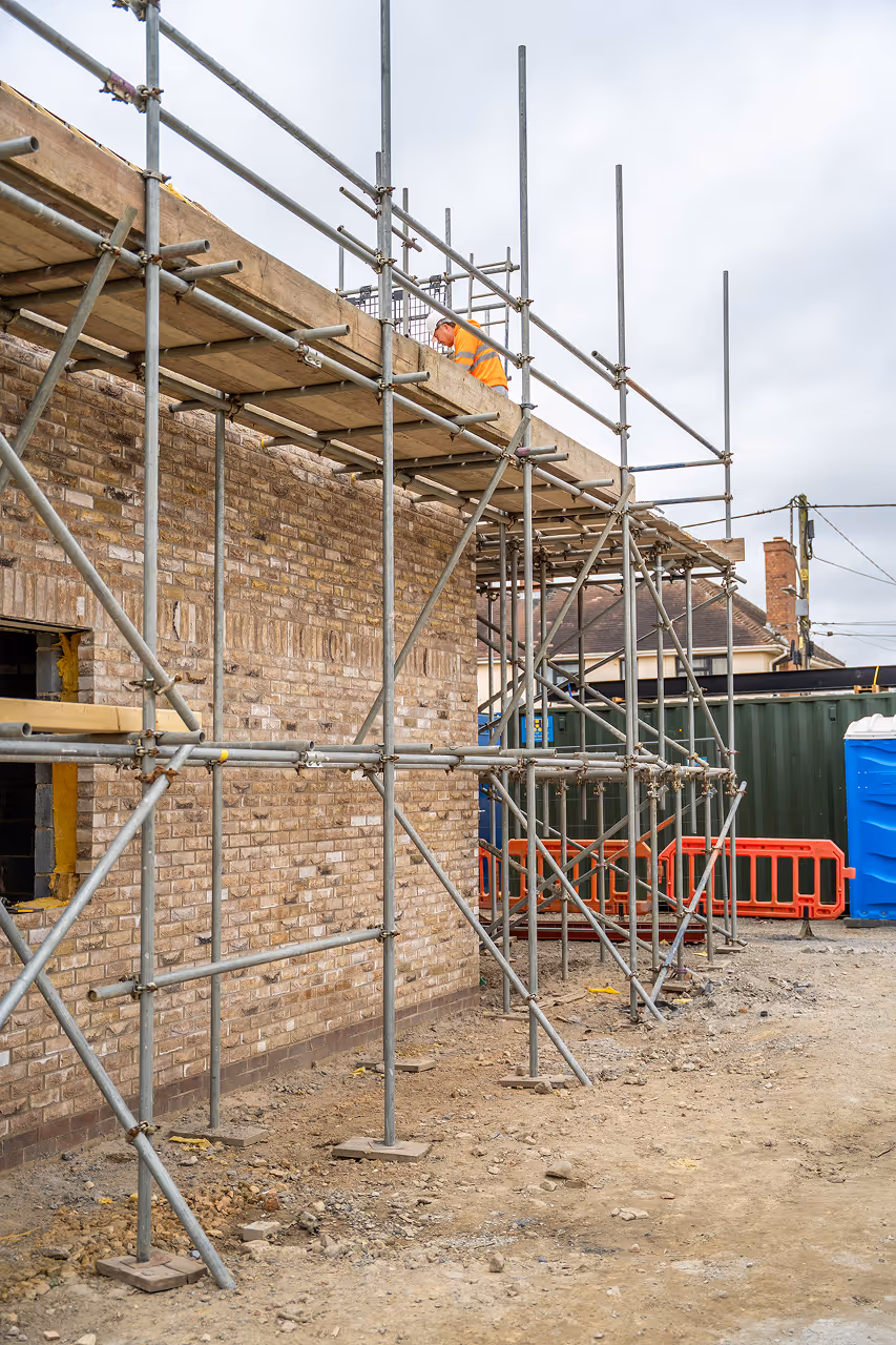 Construction work and scaffolding on a brick building under cloudy sky.