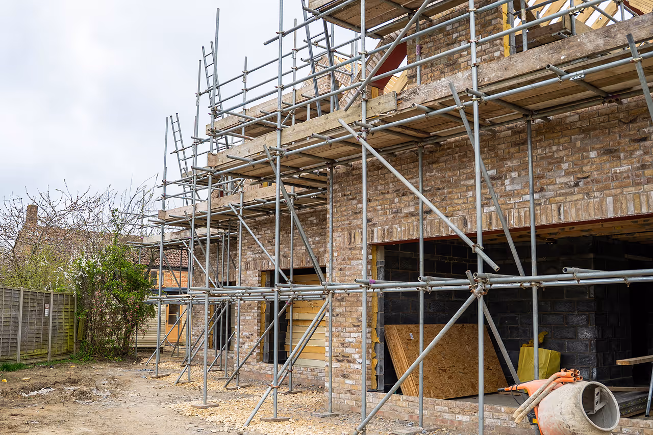 Brick house under construction with metal scaffolding and building materials around it.