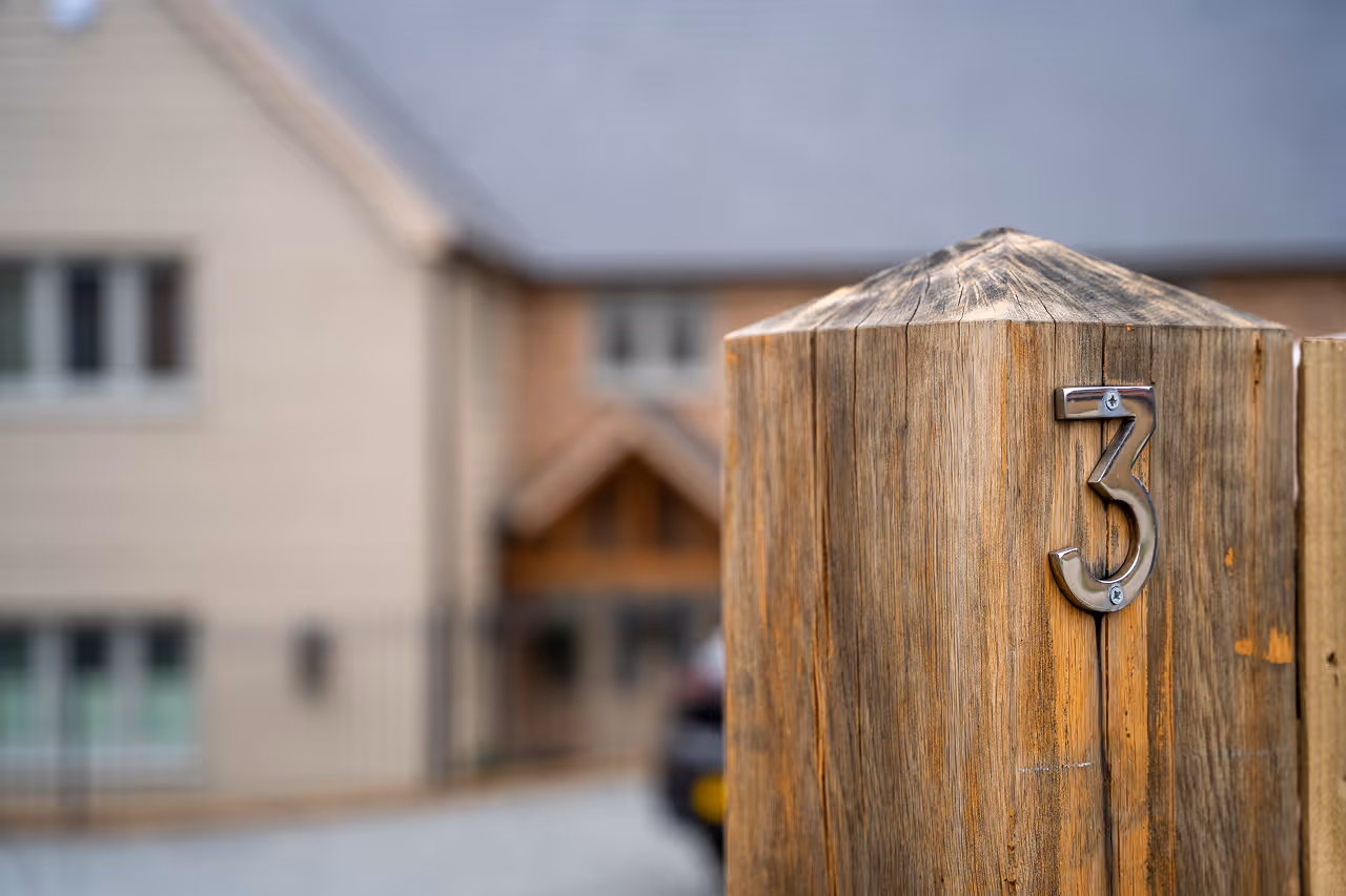Metal number 3 mounted on a wooden post with a blurred house and driveway in the background.