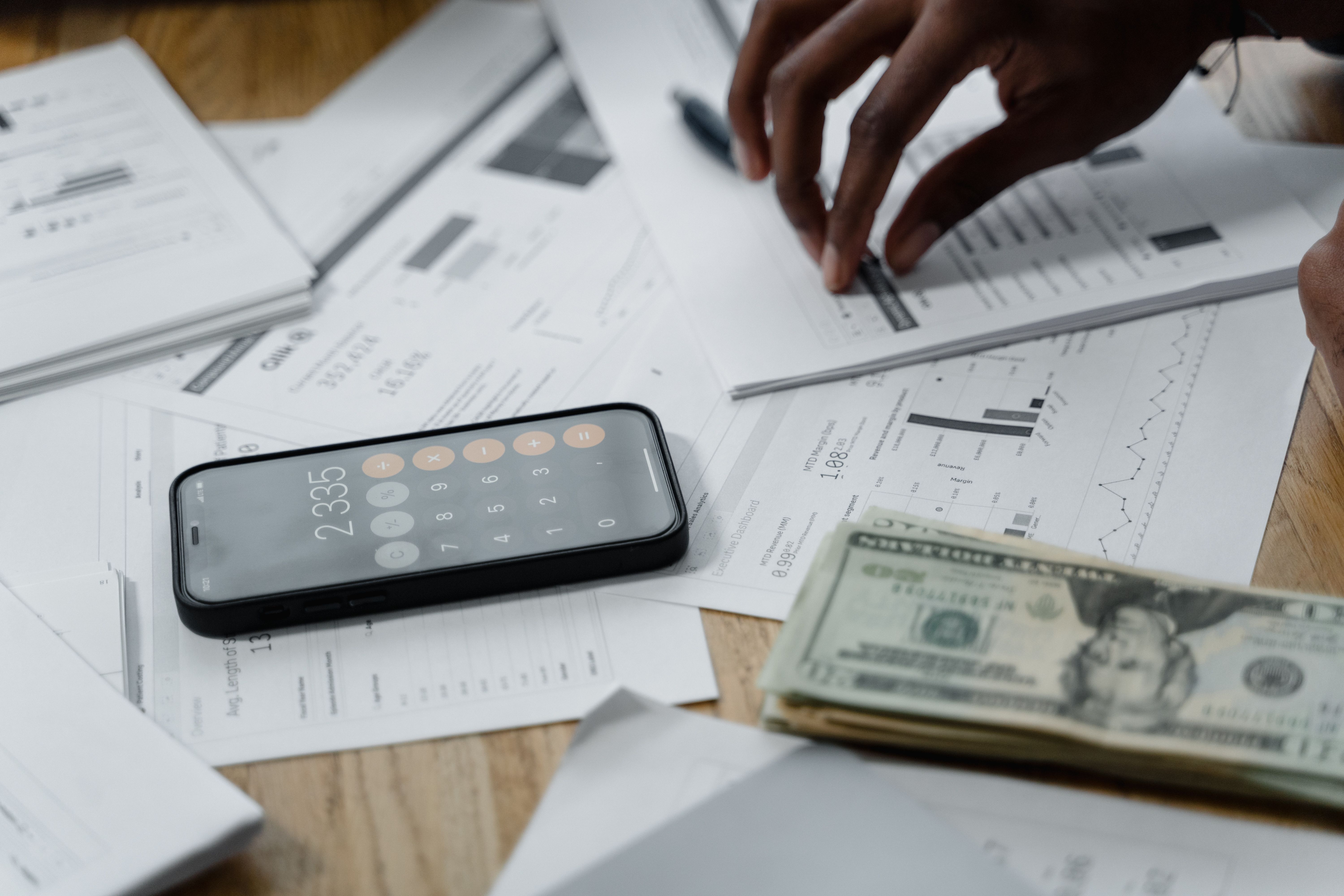 Persona calculando el costo de una remesa con dólares y un teléfono
