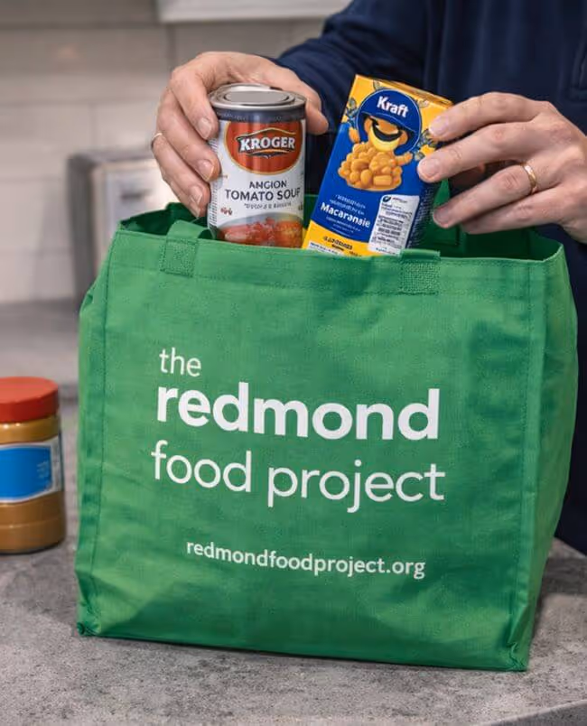 A green bag on a countertop being filled with non-perishable donated food.
