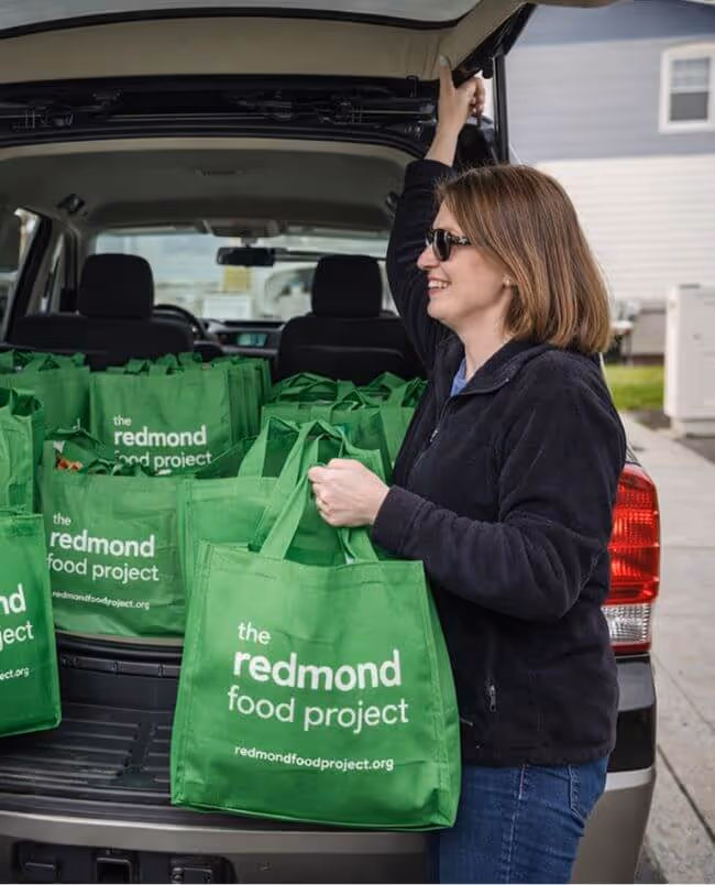 A woman unloading green bags from the back of her SUV.
