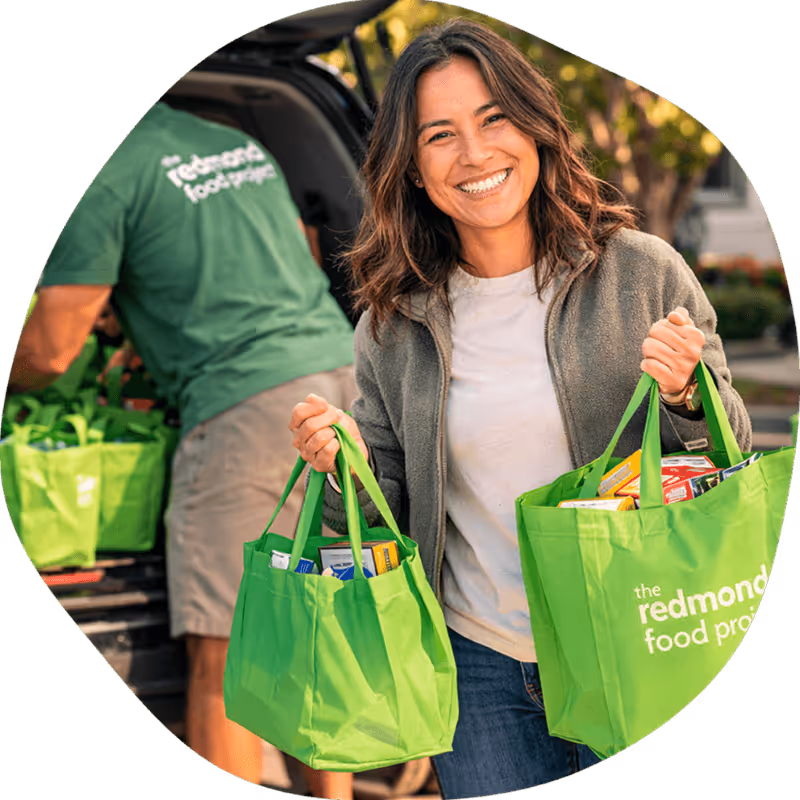 A female volunteer unloading green bags of donated food for The Redmond Food Project.