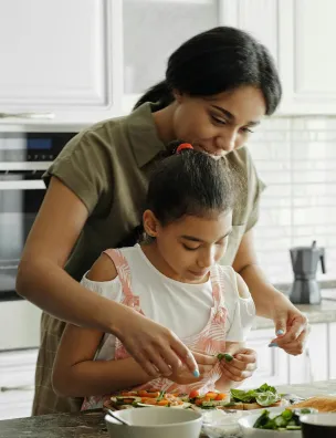 Woman and girl preparing and decorating a salad together in a kitchen.