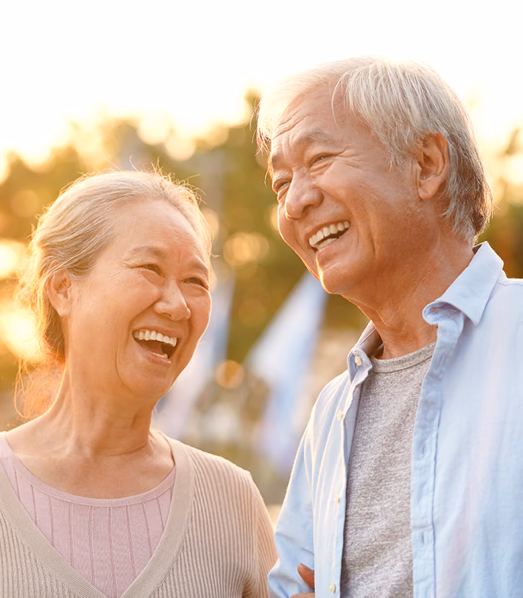 Elderly man and woman smiling and laughing outdoors at sunset.