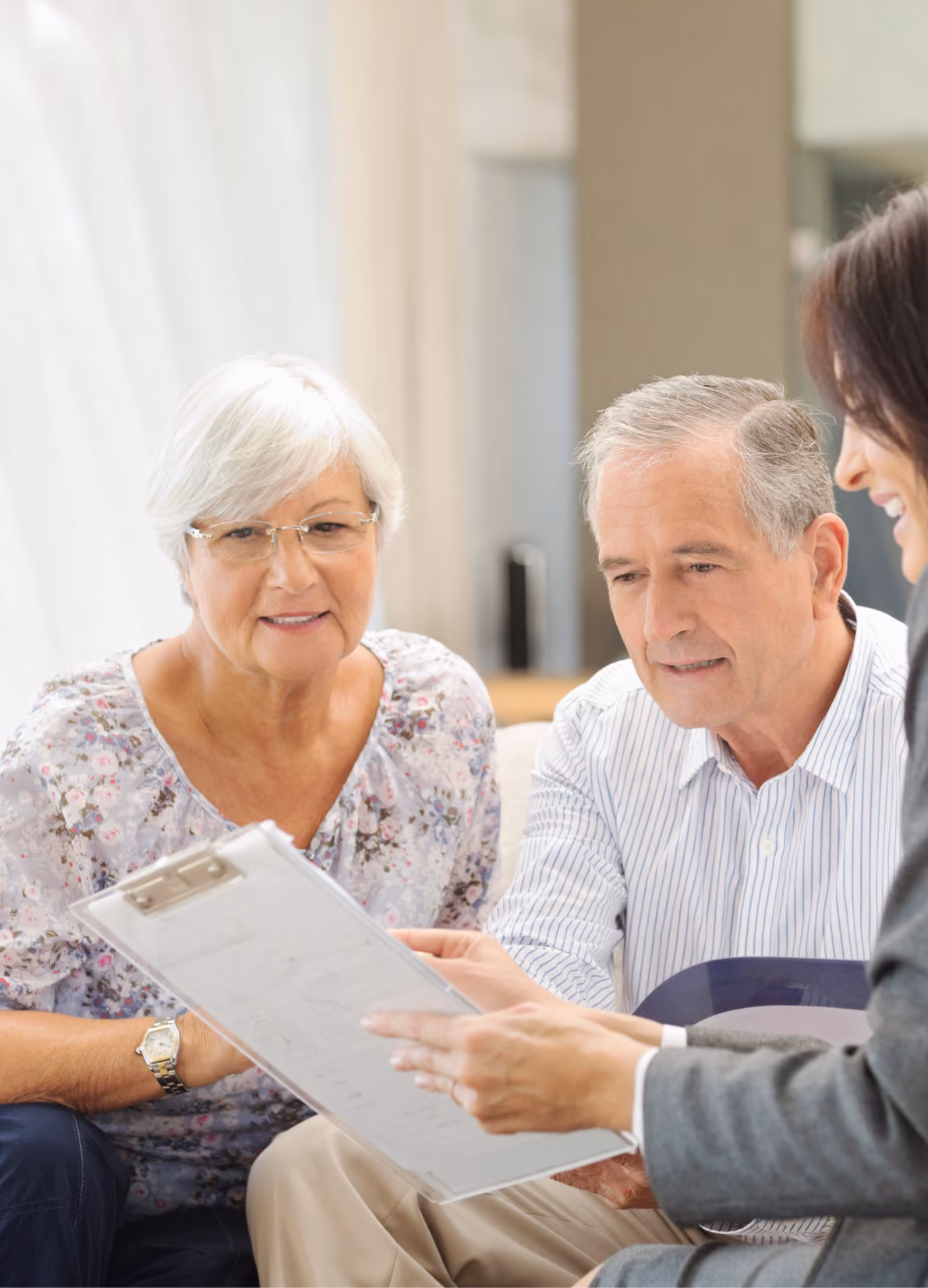 An elderly couple attentively reviewing a document on a clipboard with a professional woman in an office.
