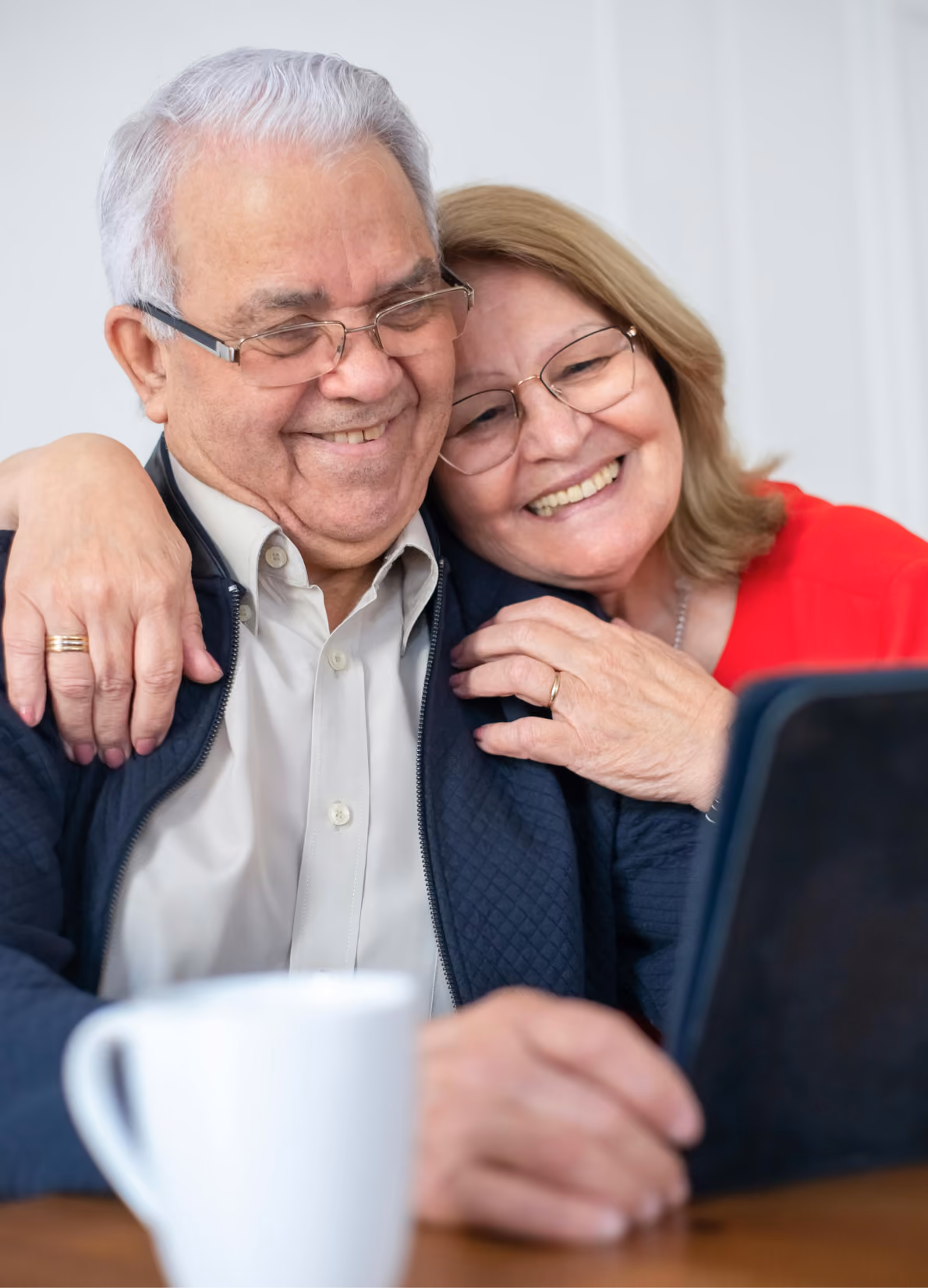 Smiling elderly couple wearing glasses hugging and looking at a laptop together.