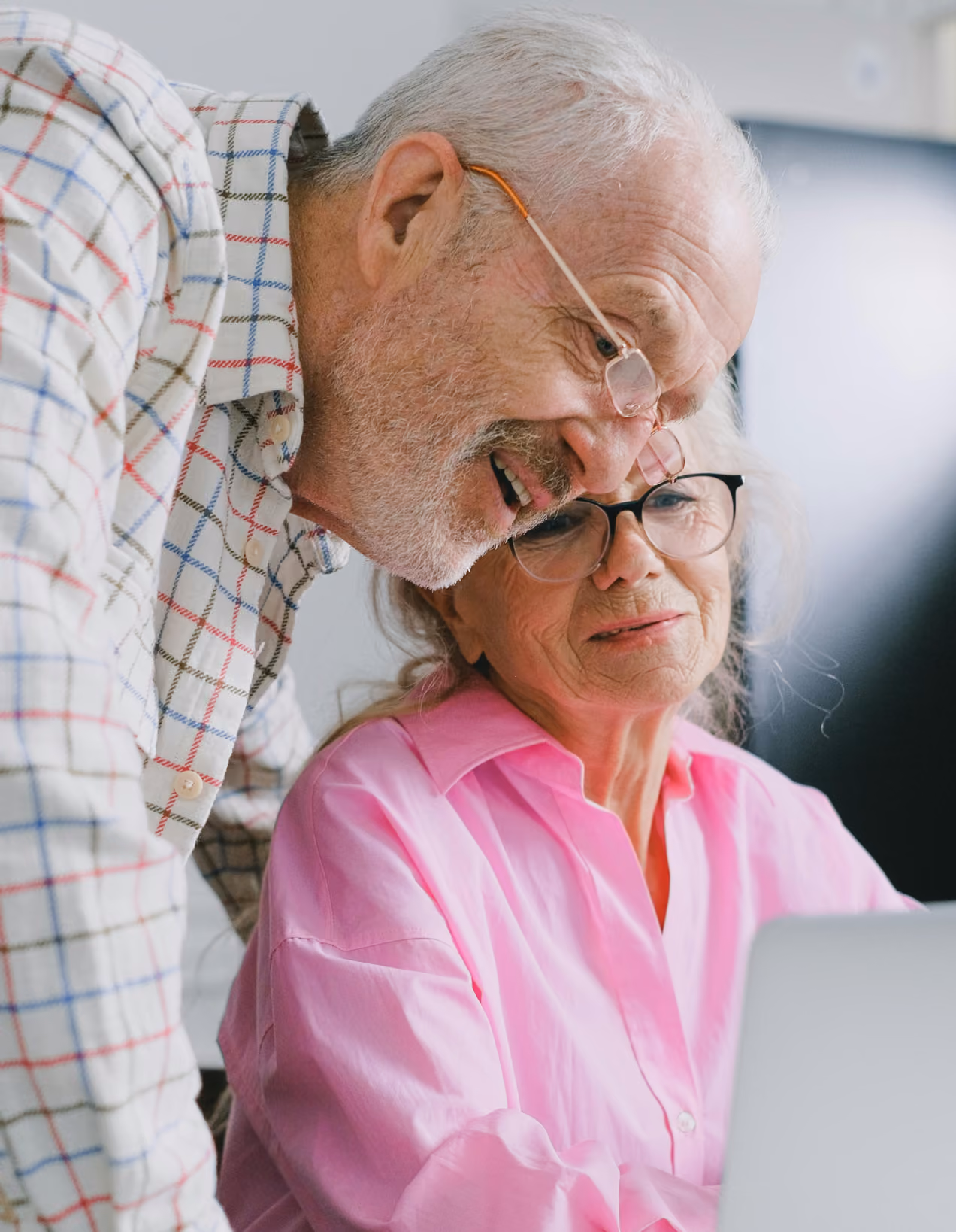 Elderly man and woman wearing glasses looking at a laptop screen together.