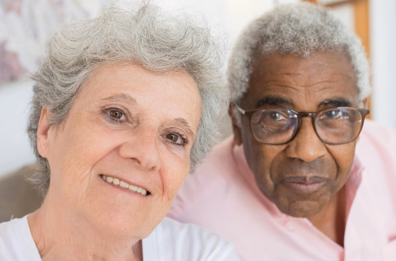 Close-up of an elderly woman smiling and an elderly man wearing glasses sitting side by side.