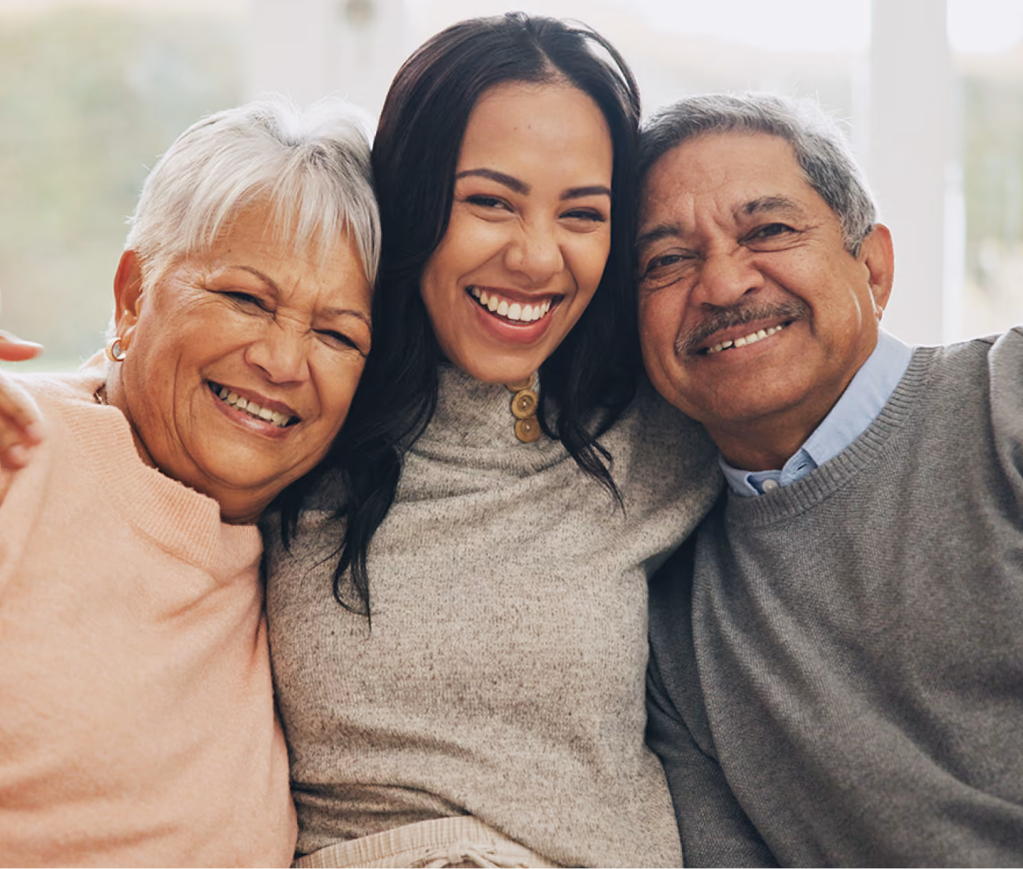 Smiling elderly woman, young woman, and elderly man sitting closely together indoors.