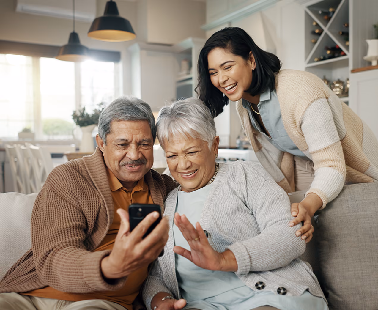 Three adults smiling and video chatting on a smartphone in a cozy living room.