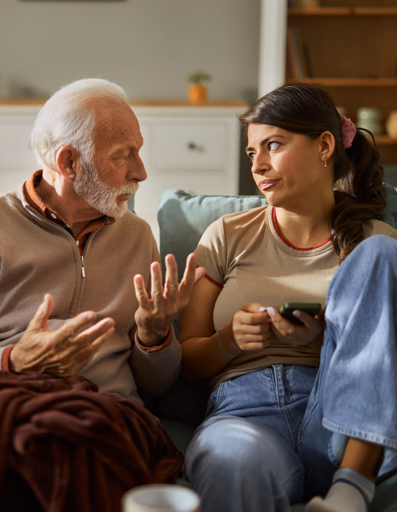 Elderly man and young woman sitting on couch having a serious conversation indoors.