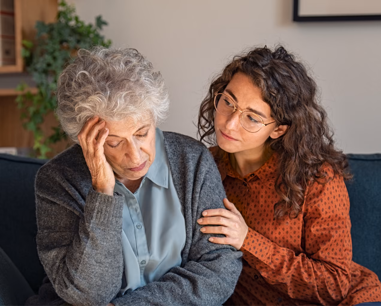 Younger woman consoling an older woman who looks distressed, sitting together on a couch.