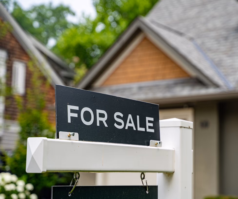 Black and white 'For Sale' sign in front of a house with blurred background.