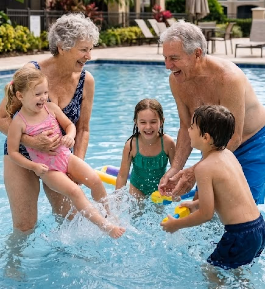 Two seniors and three children happily playing and splashing water in a swimming pool.