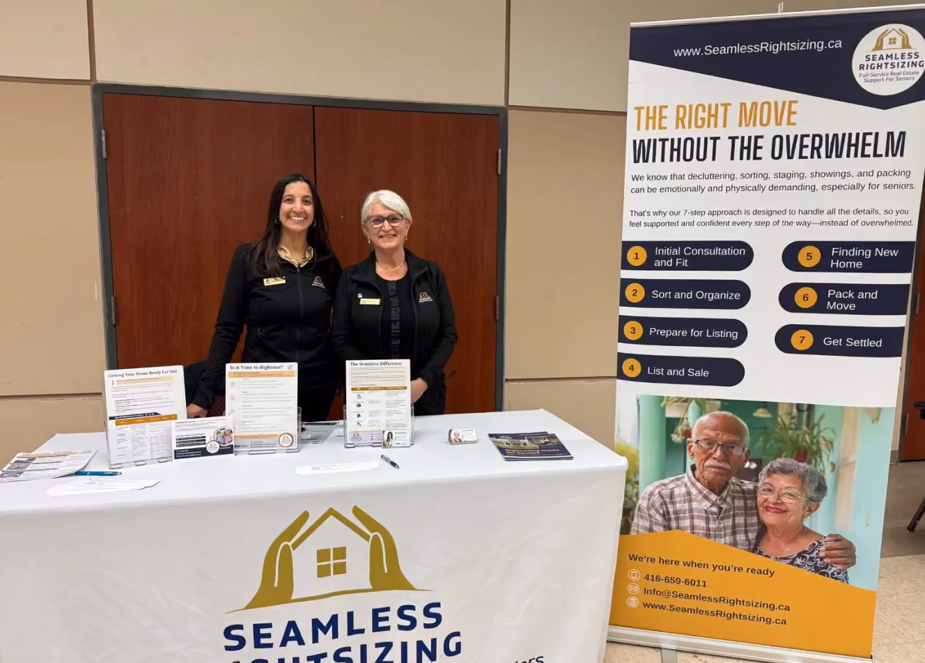 Two smiling women stand behind a Seamless Rightsizing info table with pamphlets and a banner.