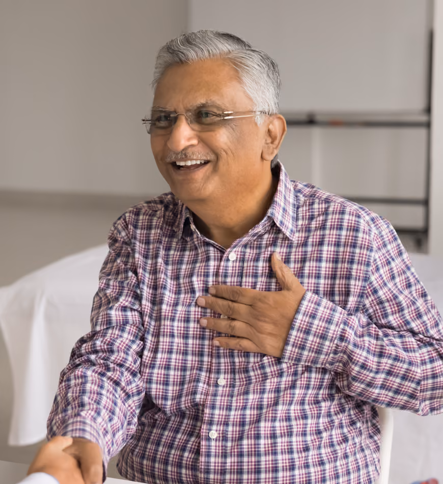 Smiling older man in glasses and plaid shirt shaking hands while placing hand on his chest.