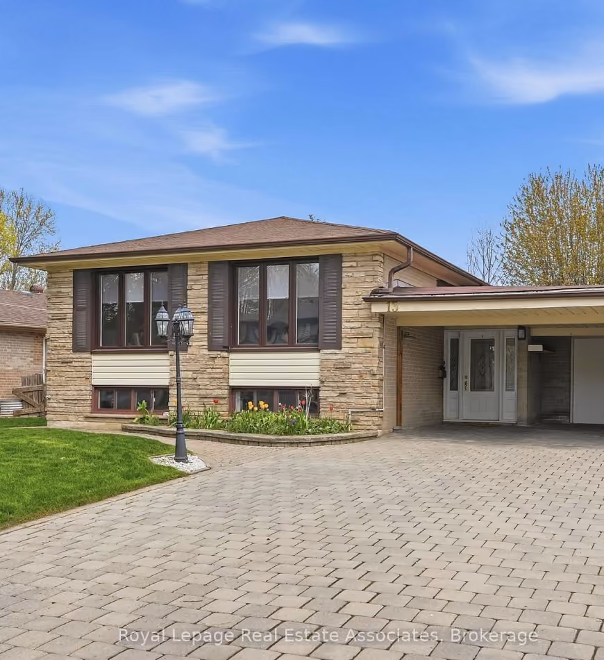 Single-story brick house with large front windows, a lamp post, flower bed, and paved driveway under blue sky.