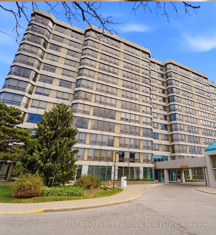 Multi-story residential building with large windows and greenery in front under a blue sky.