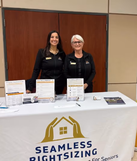 Two smiling women stand behind a Seamless Rightsizing table with informational brochures.