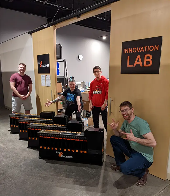 The TCG Machines team poses with the first four production PhyzBatch-9000 trading card sorting robots