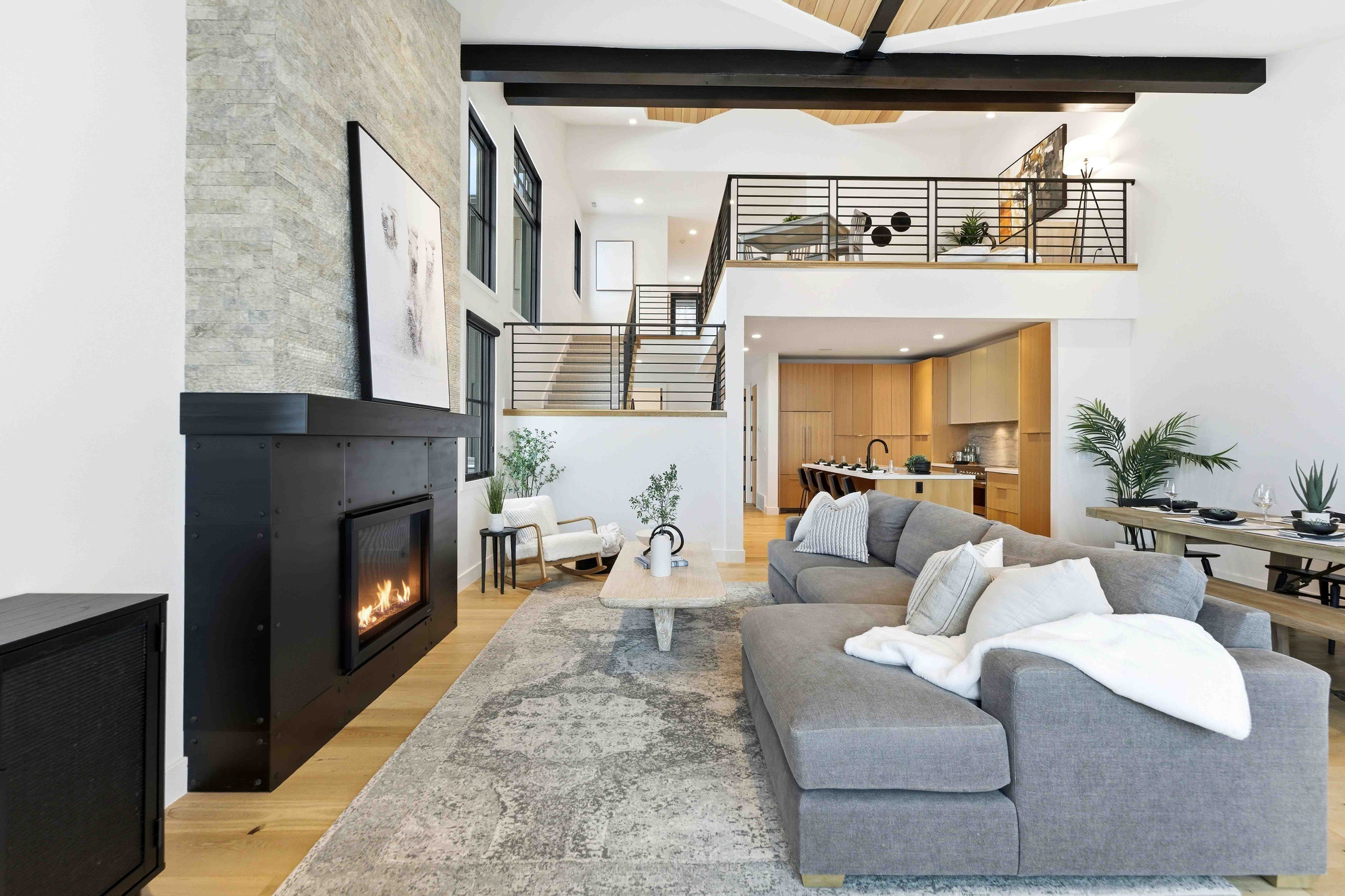 Modern living room with gray sectional sofa, fireplace, light wood flooring, and open kitchen with dining area.