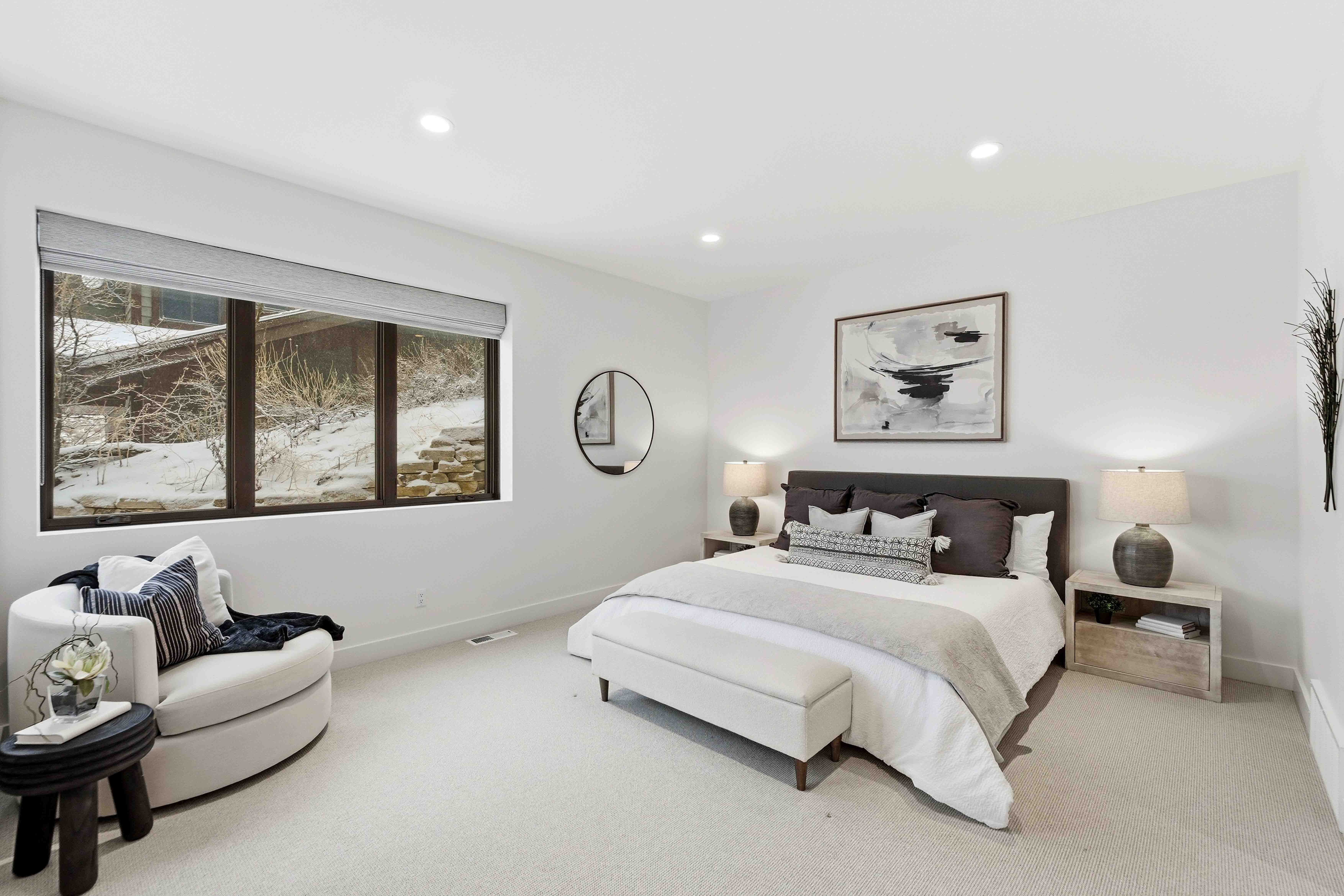 Modern white bedroom with a large bed, round chair by window showing a snowy outdoor scene.