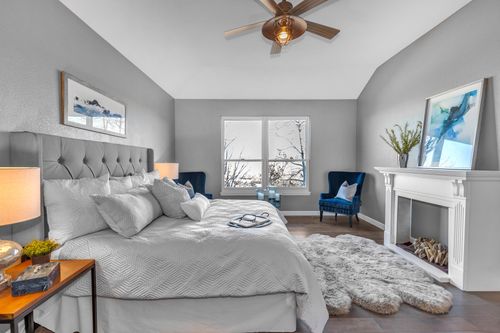 Bright bedroom with gray tufted bed, blue armchairs, white fireplace, and a fluffy rug on wood floor.