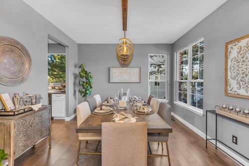 Modern dining room with wooden table set for eight, beige and gray chairs, and large windows.