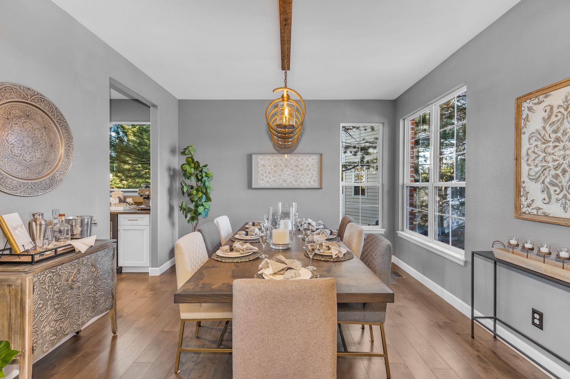 Modern dining room with wooden table set for eight, beige and gray chairs, and large windows.